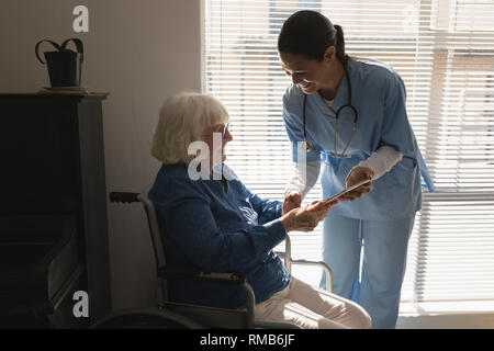 Female doctor discussing medical report with disable senior woman on digital tablet Stock Photo