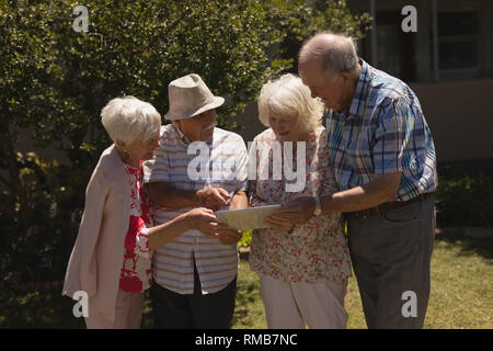 Front view of senior friends discussing over digital tablet in garden Stock Photo