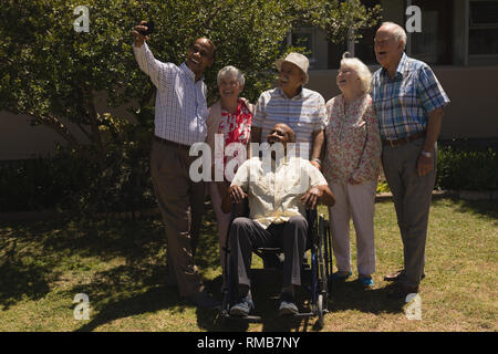 Front view of senior friends taking selfie with mobile phone in garden Stock Photo
