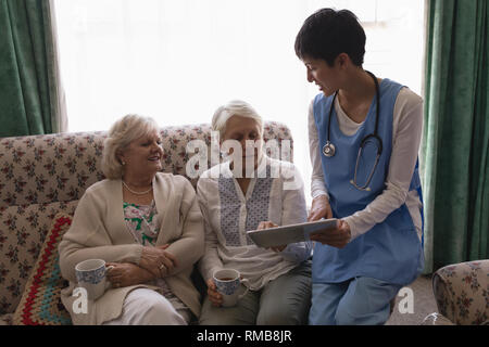 Female doctor and senior women discussing over digital tablet in living room