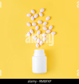 Pills dropped from bottle on yellow background. Flat lay, top view. Stock Photo