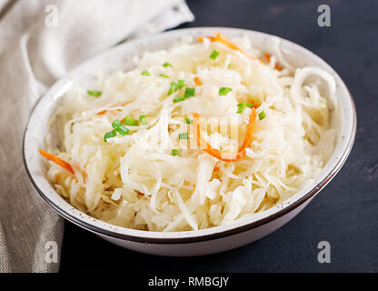 Fermented cabbage. Vegan food. Sauerkraut with carrot and spices in bowl on the dark background. Trend food. Stock Photo