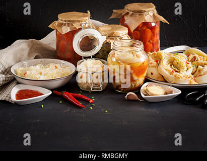 Fermented food. Vegetarian food concept. Cabbage kimchi, tomatoes marinated, sauerkraut sour glass jars over rustic kitchen table. Canned food concept Stock Photo