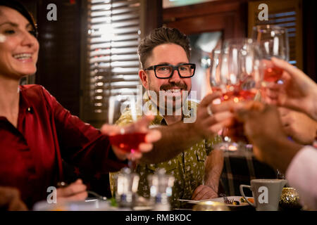 Cheerful mature man raising his glass for a celebratory toast with her friends while sitting in a restaurant having a meal. Stock Photo