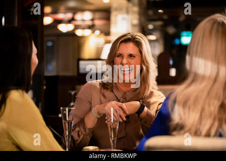 Over the shoulder view of a mature woman laughing and smiling with her friends while sitting in a restaurant. Stock Photo
