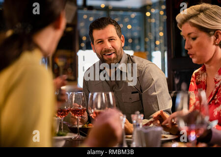 Mid adult man sitting at a restaurant table with some friends and enjoying a meal. Stock Photo