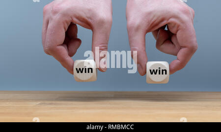 Symbol for a win win situation. Hands are holding two dice with the words "win" and "win" in front of a grey background. Stock Photo