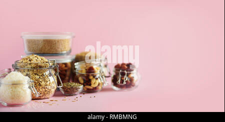 Grains, cereals, nut, dry fruits in glass jars over pink background with copy space. Clean eating, healthy, vegan diet concept. Stock Photo