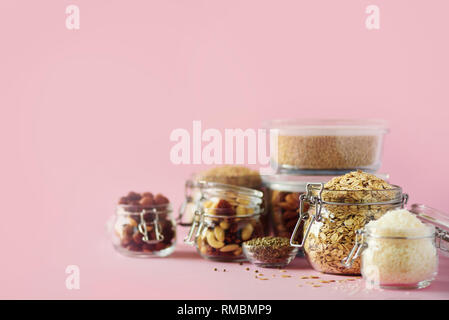 Grains, cereals, nut, dry fruits in glass jars over pink background with copy space. Clean eating, healthy, vegan diet concept. Stock Photo