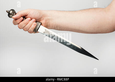 Male hand holds an old roman dagger, isolated  on the white background. Stock Photo