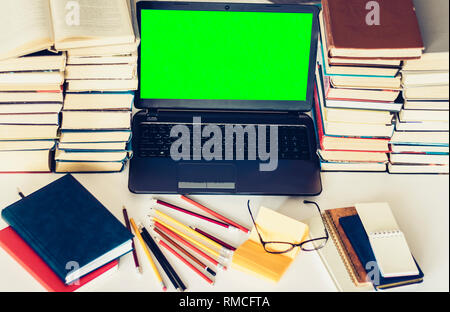 Green screen laptop, stack of books, notebooks and pencils on white table, education office concept background Stock Photo