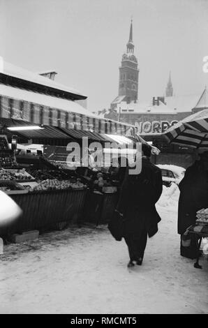 View of the Munich Viktualienmarkt in winter. In the background is a shop of the restaurant chain Nordsee as well as the steeples of St. Peter and Holy Spirit Church. Stock Photo