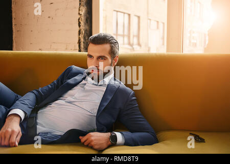 Feeling confident...Relaxed handsome young businessman in stylish suit is resting in sofa at office and thinkg about business. Fashion look. Business  Stock Photo