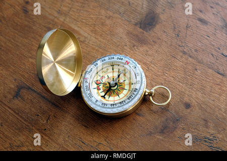 Old compass in opened brass case on vintage brown wooden background shown to North direction top view close up Stock Photo