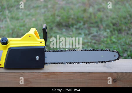 New black and yellow electric saw on brown wooden balk ready for work outdoors closeup view Stock Photo