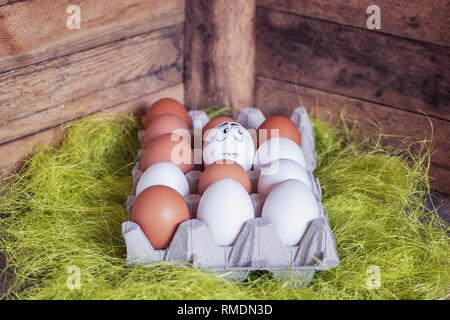 Easter composition with white and brown eggs in a box where one egg has a sad face because it is broken. Stock Photo