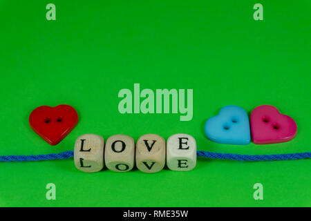 Red and blue heart shaped buttons and word Love on blocks threaded on strings over a colorful green background for romantic or Valentines concepts wit Stock Photo