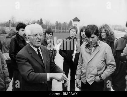 Adolf Meislinger, former concentration camp prisoner, leads teenagers, presumably of the Aktion Suehnezeichen (Action Reconciliation) through the Dachau Concentration Camp probably in 1985. In the background, a concentration camp watch tower. Stock Photo