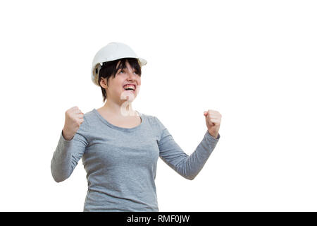 Excited young woman engineer wearing protective helmet holding fists tight raising hands looking up celebrating success isolated over white background Stock Photo