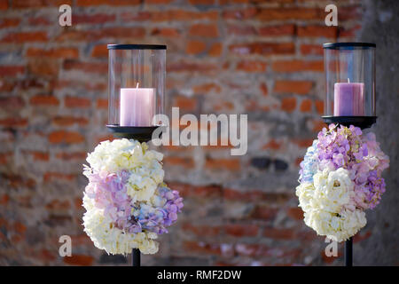 Minimalist outdoors two candle holders with pastel colored hydrangeas bouquets at the basis, decorative element for a formal event or a wedding Stock Photo