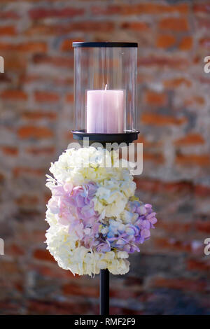Minimalist outdoors one candle holder with pastel colored hydrangeas bouquets at the basis, decorative element for a formal event or a wedding Stock Photo