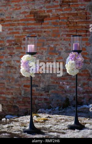 Two outdoors free-standing candle holders with pastel colored hydrangeas bouquets at the basis, decorative element for a formal event or a wedding Stock Photo