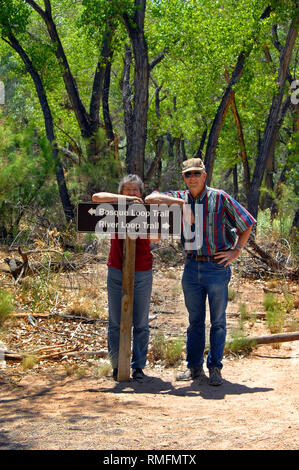 Senior couple lean on sign at the Rio Grand Nature Center State Park in Albuquerque, New Mexico.  Couple are deciding which trail to take. Stock Photo