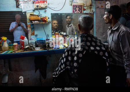 At an open-air hairdresser's in Mumbai, India, hairdresser & customer are mirrored while in serious mood, the photographer seen in another mirror Stock Photo