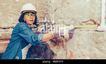 Clever woman repairing her bathroom pipes with  positive attitude. Woman using leveling tool while setting up and checking the tubes in the bathroom. Stock Photo