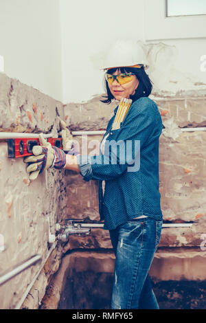 Clever woman repairing her bathroom sink pipe with  positive attitude. Woman using leveling tool while setting up and checking the tubes in the bathro Stock Photo