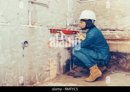 Clever woman repairing her bathroom pipes with  positive attitude. Woman using leveling tool while setting up and checking the tubes in the bathroom. Stock Photo