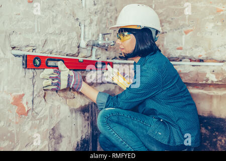 Clever woman repairing  bathroom pipes with  positive attitude. Woman using leveling tool while setting up and checking the tubes in the bathroom. Stock Photo