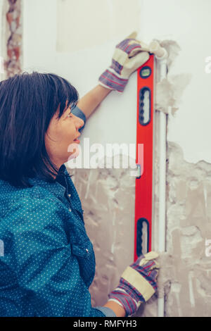 Clever woman repairing her bathroom pipes with  positive attitude. Woman using  Bubble Spirit Water Ruler Tool while setting up and checking the tubes Stock Photo