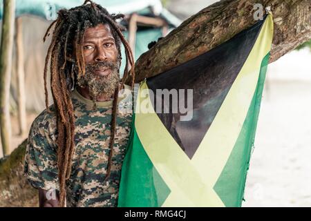 African American bearded male with dreadlocks holding Jamaica flag near tree Stock Photo