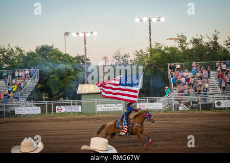 Texas cowgirl riding horseback with American flag. Opening ceremony at small town rodeo Stock Photo