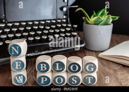 words NEW BLOG POST on wooden blocks against vintage typewriter, potted plant and note pad on table. Stock Photo