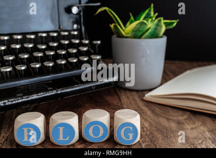 word BLOG on wooden blocks against vintage typewriter, potted plant and note pad on table Stock Photo