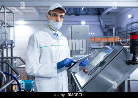 man in a white robe and a mask with a tablet in his hands is near can in the shop Stock Photo