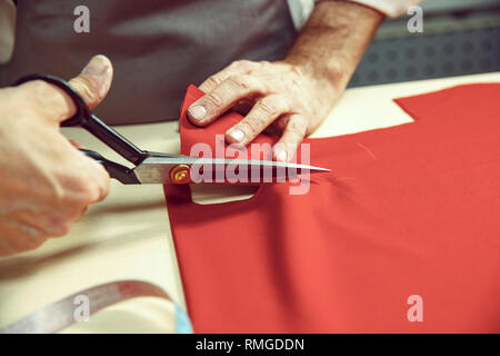 Closeup of tailors table with male hands tracing fabric making pattern for clothes in traditional atelier studio. The man in female profession. Gender equality concept Stock Photo
