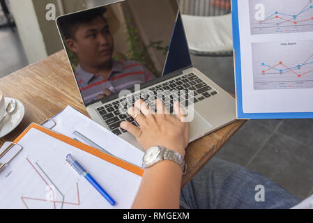 Asian man reading financial document and using laptop Stock Photo
