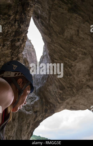 Profile of a woman climber, from the side, wearing a blue helmet, just beneath a rock cave called Hilli's Cave, in Turda Gorge (Cheile Turzii) Romania Stock Photo