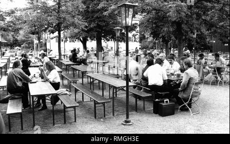 Some guests sit on the beer benches of the beer garden Aumeister in the English Garden in Munich.