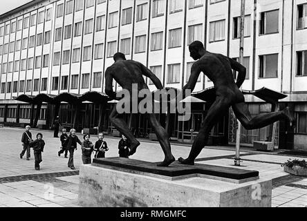 At the square in front of the DHfK in Leipzig a plastic has been set up. The sculpture shows two relay runners, one of them hands over the baton to the other. Children are looking at the artwork. Art in architecture. Stock Photo