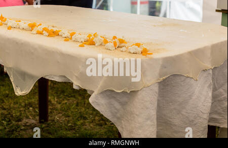 Homemade strudel dough on a traditional linen tablecloth ready for making cottage cheese pie and other pastry. Ingredients of the filling - cottage ch Stock Photo