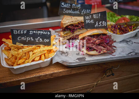 Salt beef bagel and sandwich with beef dipping chips on a wooden board on sale at a street food stall in a local farmer market. Landscape format. Stock Photo