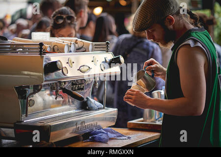 London, UK - June, 2018. A barista preparing a latte at a stall in Borough Market, one of the oldest and biggest food market in London. Stock Photo