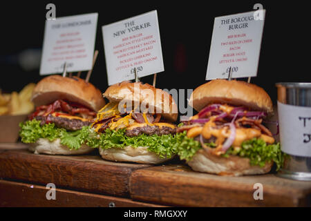 Three beef burgers with cheese, bacon, lettuce, onions and pickles on sale at a street food stall in a local farmer market. Food concept. Stock Photo