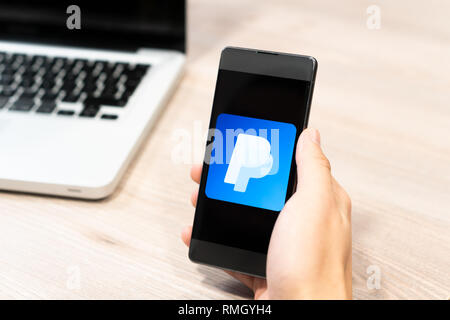 Human hand holding mobile phone - paypal logo displayed on phone,, computer laptop in the background. Slovenia 13.02.2019 Stock Photo