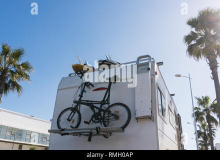 RV White Camper Car with bicycles on Road surrounded with Palm trees. Driving and cycling lifestyle Stock Photo