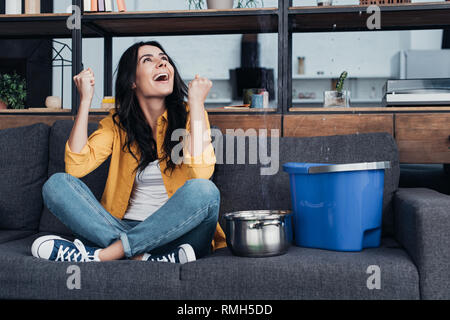 Laughing woman in jeans sitting on sofa and looking up Stock Photo